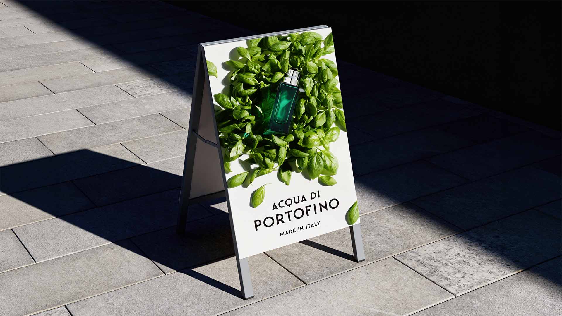 Metal A-frame pavement sign on a stone walkway displaying Acqua di Portofino campaign visuals.