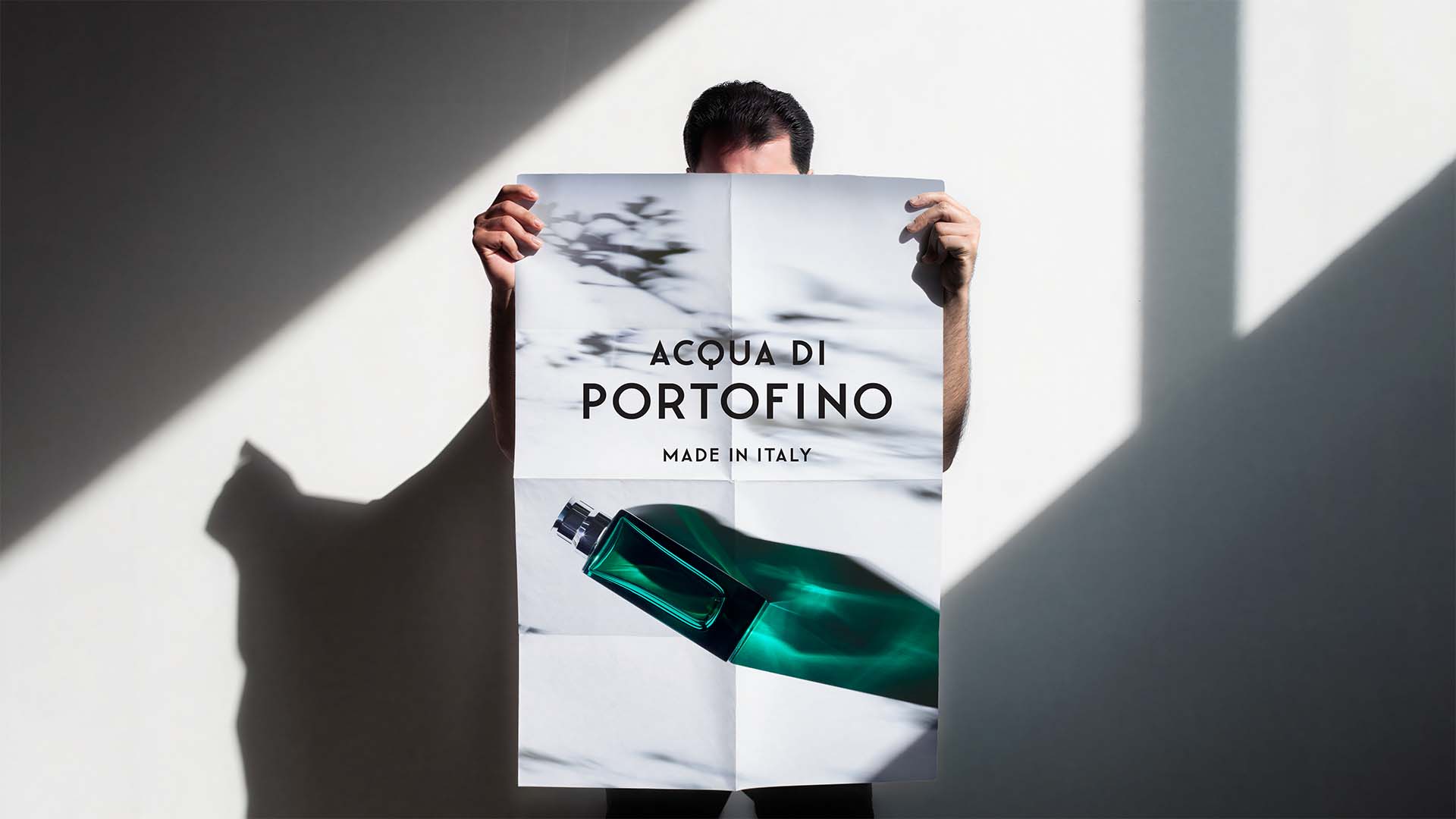 Person holding a large quad-folded campaign poster featuring emerald green fragrance bottle photography.