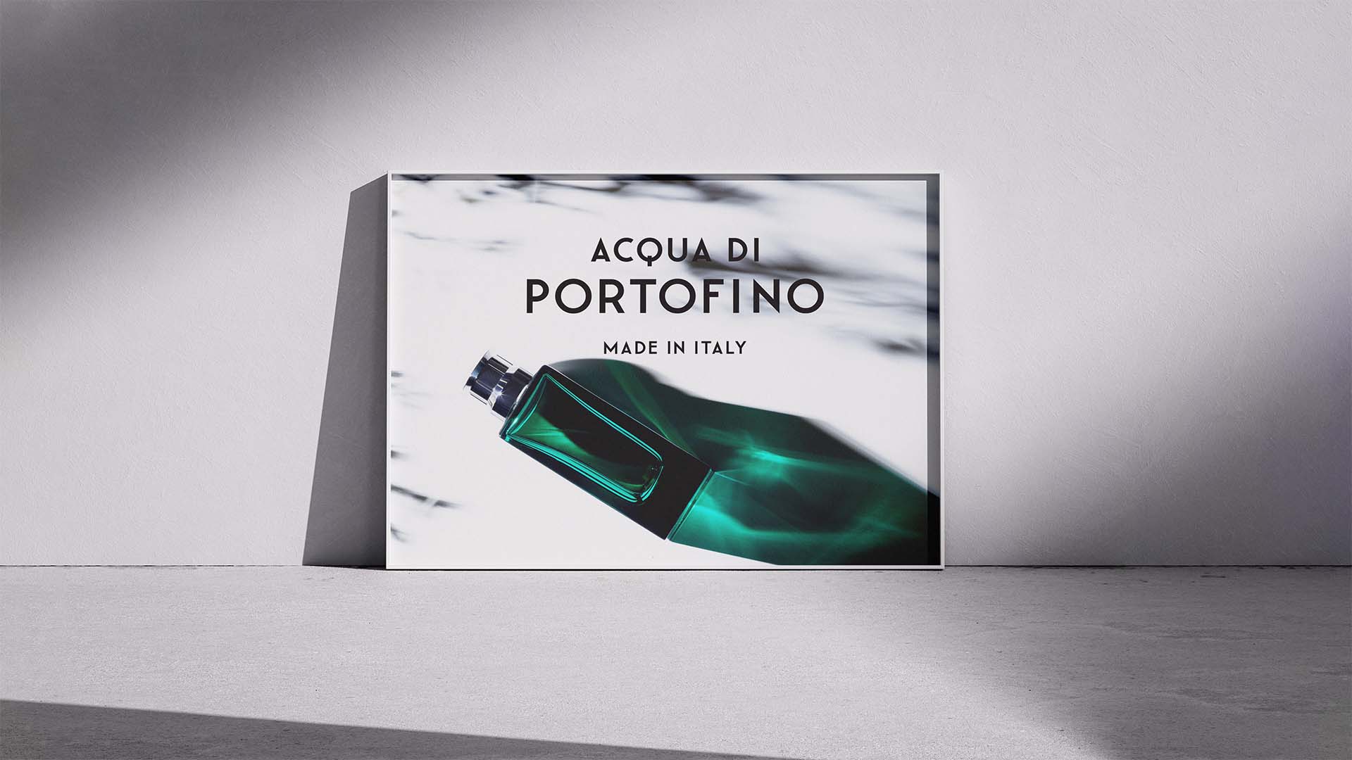 Framed advertising poster leaning against a wall showing an emerald perfume bottle and light refractions.