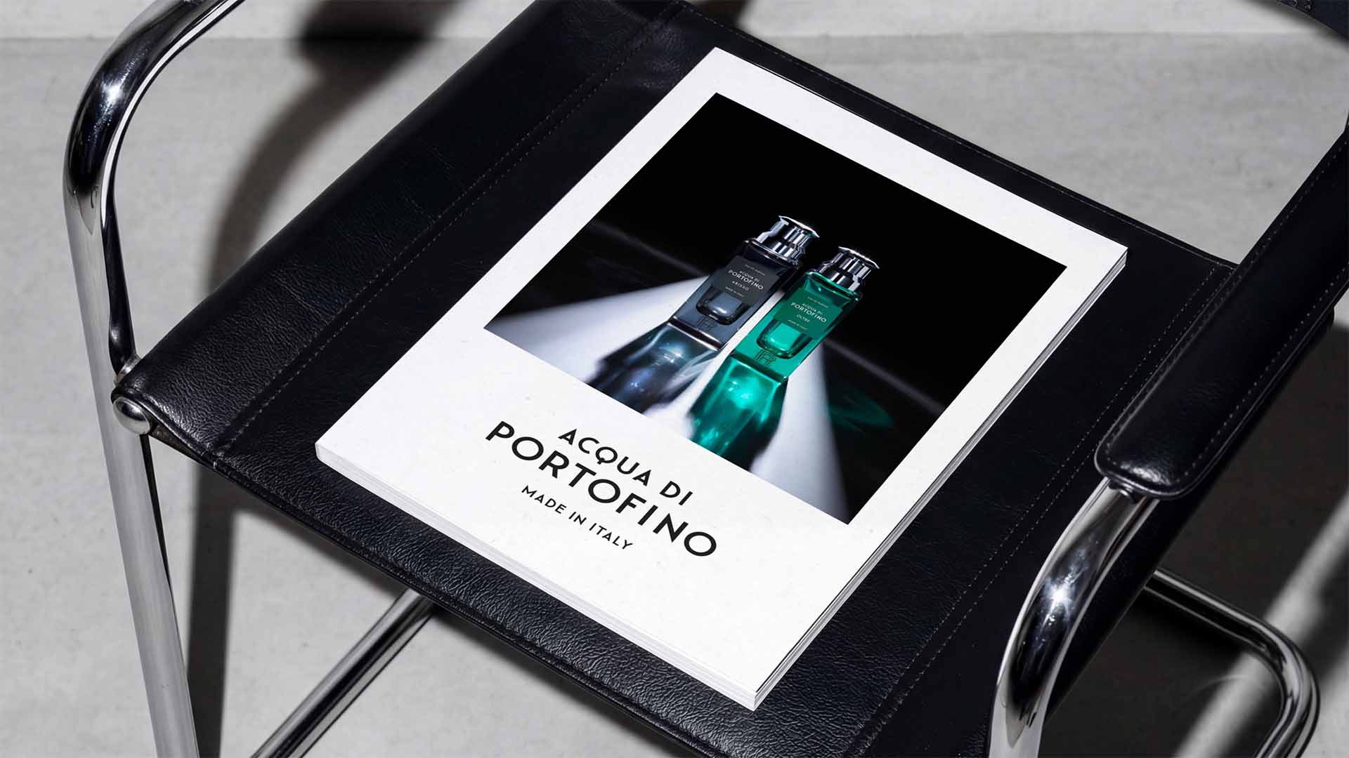 Hardcover brand publication catalog resting on a modern black leather and tubular chrome arm chair.