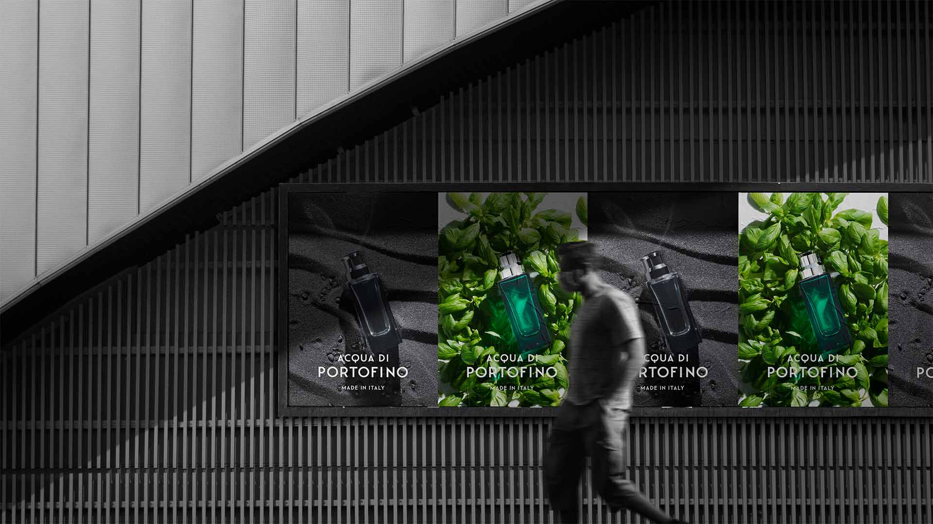 Pedestrian walking past repeating transit advertising posters displaying dark Acqua di Portofino campaign visuals.