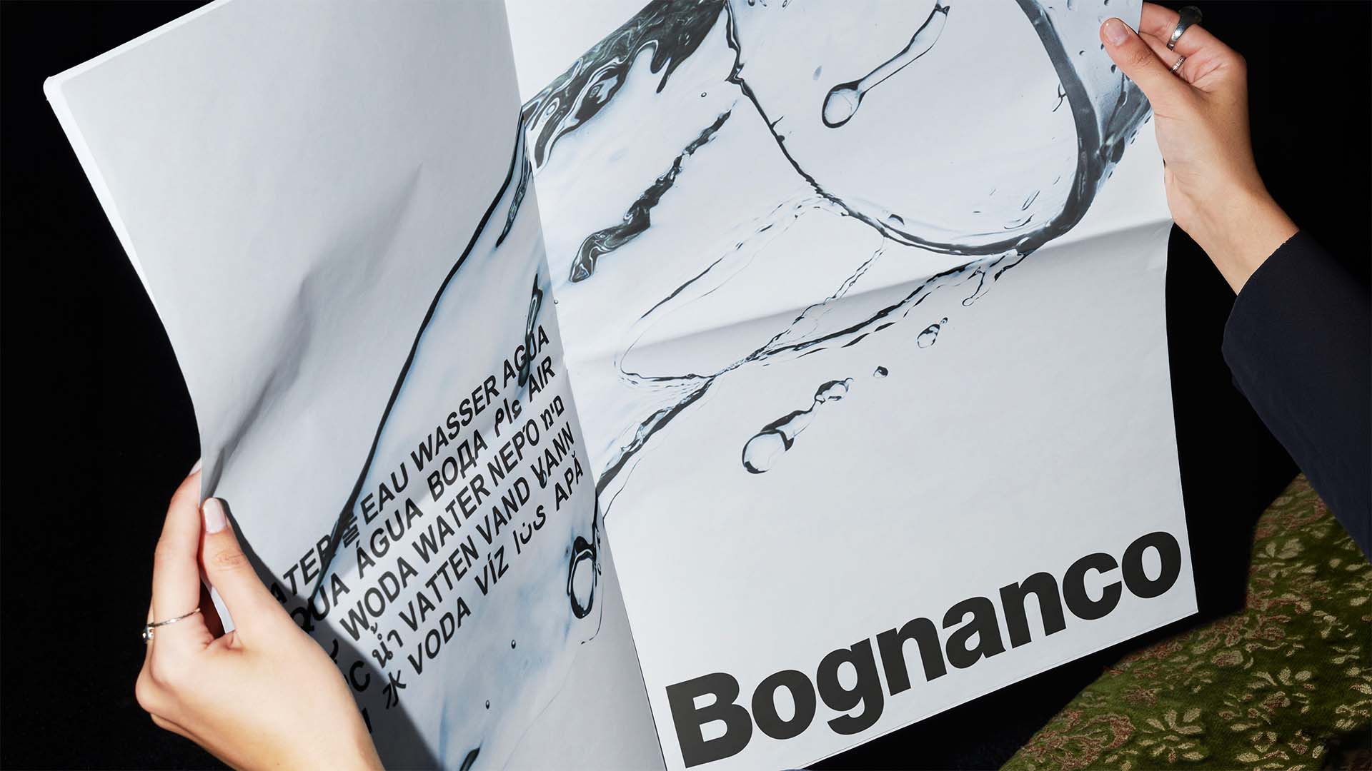 Hands holding a double-page newspaper print advertisement featuring documentary water imagery and bold typography.
