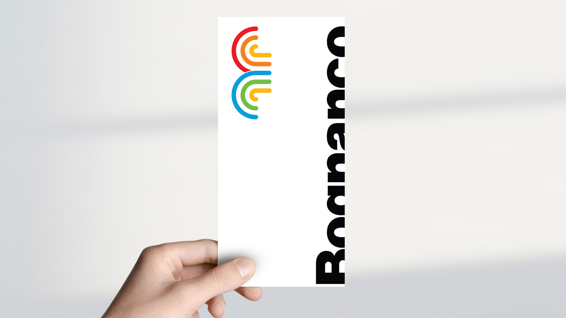 Hand holding a tall vertical white compliment card printed with colorful fountain mark and side typography.