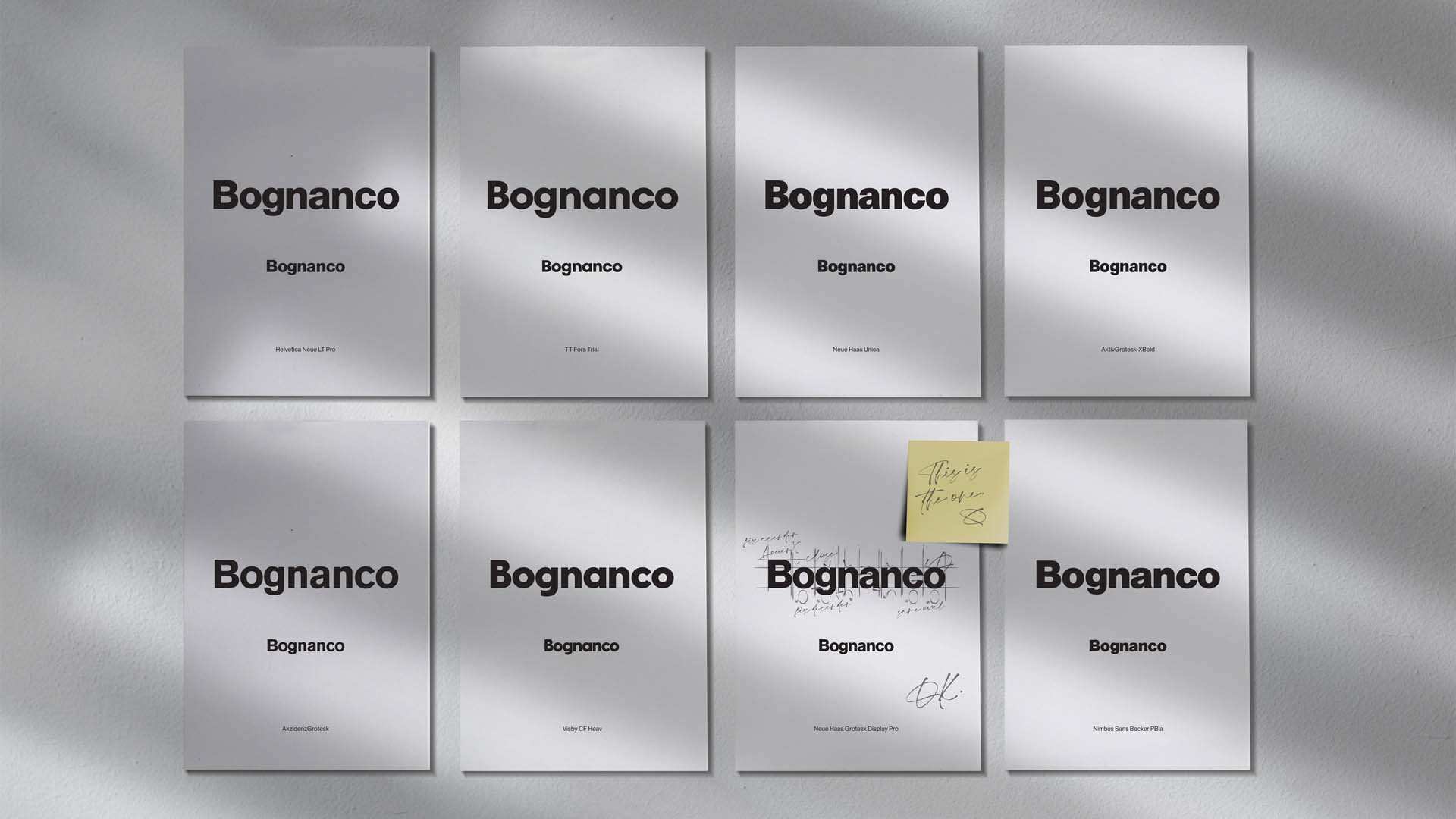 Grid of typographic exploration prints pinned to studio wall with handwritten markup and sticky note selection.